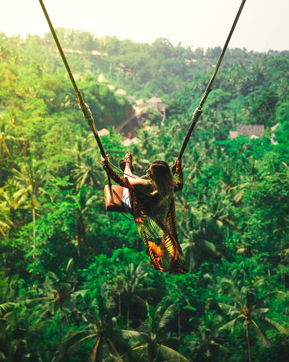 A traveler on a jungle swing high above palm trees in Bali