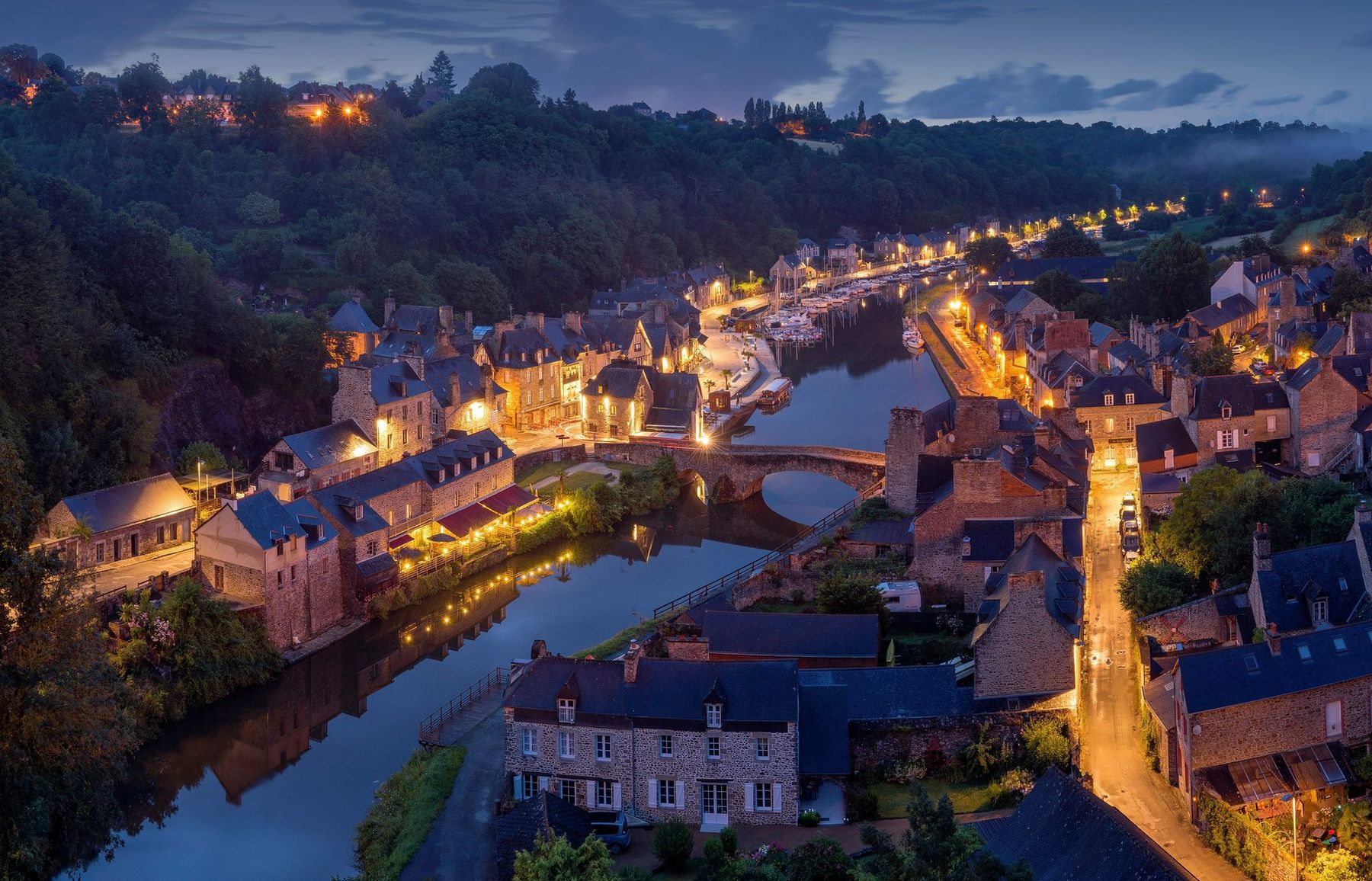 The old stone port town of Dinan, France, glowing at dusk along the Rance river