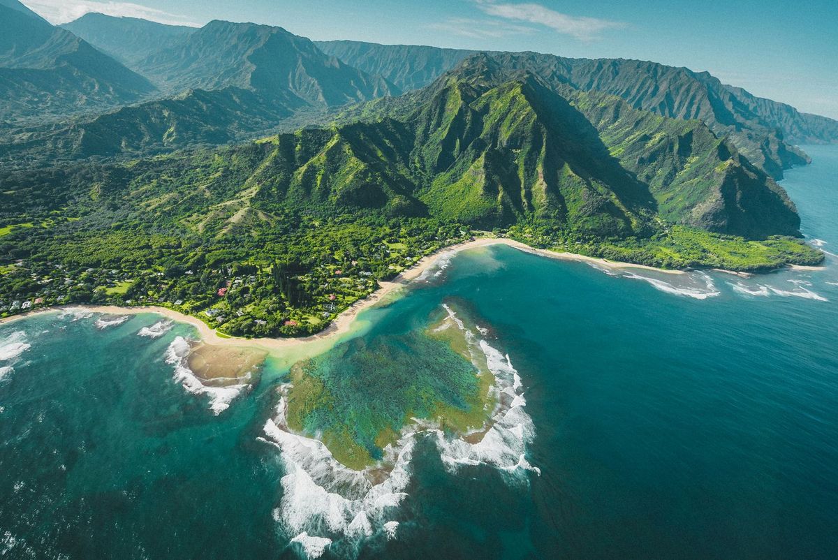 An aerial view of green mountains meeting the coast and a reef on Kauai, Hawaii