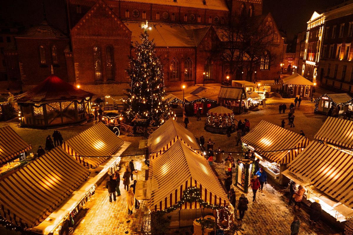A glowing Christmas market with striped stalls and a tree in front of the cathedral in Riga, Latvia