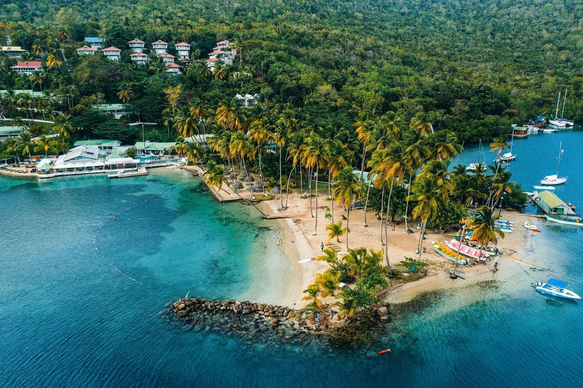 An aerial view of Marigot Bay, Saint Lucia, with a palm-covered sandbar and forested hills