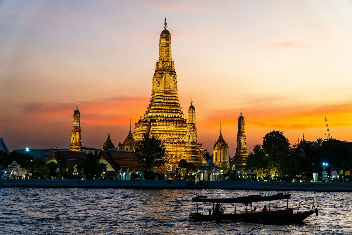 Wat Arun lit up at sunset on the river in Bangkok, Thailand