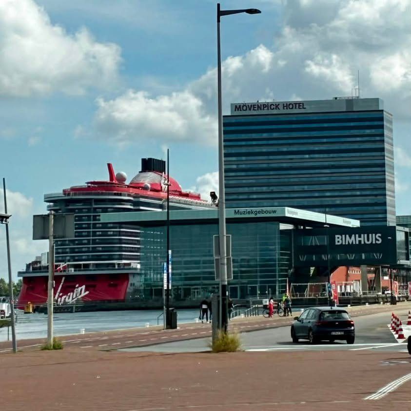 A Virgin Voyages ship docked in Amsterdam under a blue sky